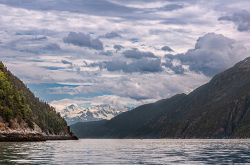 Skagway, Alaska, USA - July 20, 2011: Taiya Inlet above Chilkoot Inlet. Cloudscape breaks blue patches over snow covered mountain at end of water in the fjord. Steep mountain flanks fall into ocean.