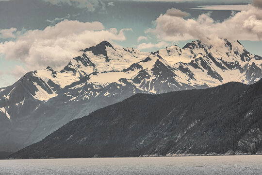 Skagway, Alaska, USA - July 20, 2011: Taiya Inlet above Chilkoot Inlet. Wide landscape with snow covered mountain along gray-gray ocean water under blue cloudscape.