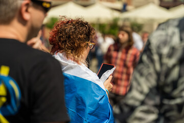 A Russian activist wearing a white-blue-white flag on her back with a phone in her hand on a sunny...