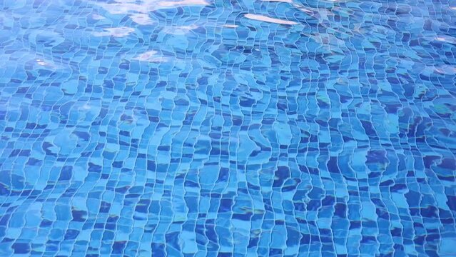 &Aacute;gua de piscina com pequenas ondas. &Aacute;gua em movimento em uma piscina de vinil com mosaico cheio de quadrados em diferentes tons de cor azul.