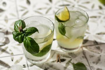 Two margarita cocktails with lime and basil in glasses close up on printed tile