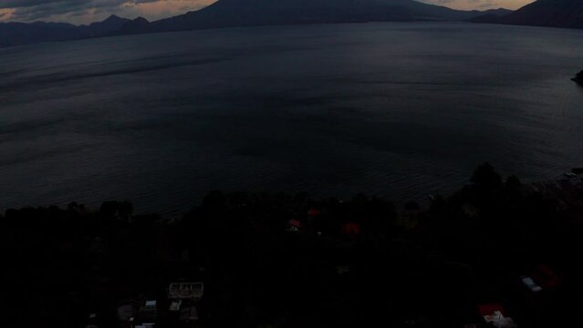 Aerial drone tilt up shot of Cerro de Oro mountain along with Lakefront houses at Night time on Lake Atitlan Guatemala, Central America.
