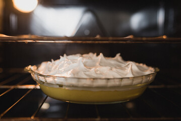 Lemon meringue pie sitting on the oven rack inside the oven; freshly baked