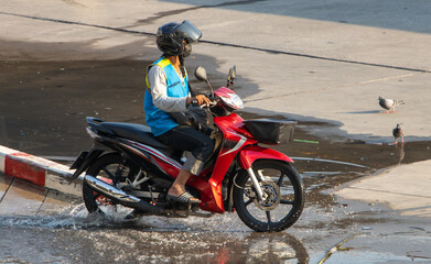 Fototapeta na wymiar The mototaxi driver in a blue vest ride on the wet street