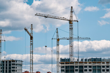 Industrial construction cranes on background of cloudy sky. Hoisting cranes and multi-storey buildings of new city districts. Building site background. Urban area.
