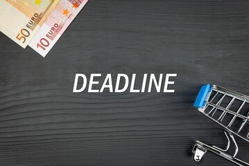 DEADLINE - word (text) and euro money on a wooden background, trolley (basket) for goods. Business concept, buying goods and products (copy space).
