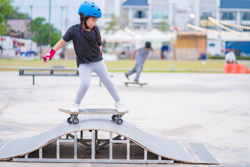 Child or kid girl playing surfskate or skateboard in skating rink or sports park at parking to wearing safety helmet elbow pads wrist and knee support - 510499053