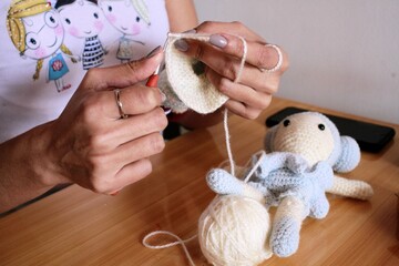 Manos de mujer tejiendo en crochet la cabeza de muñeca bailarina según modelo terminado