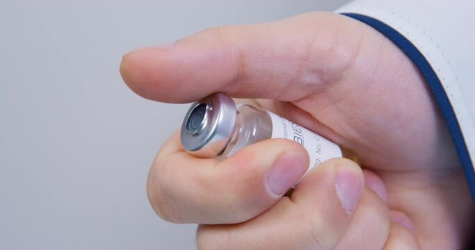 Doctor removes protective seal from glass vial of rabies vaccine, holding it in one hand, close up. Veterinarian is going to give injection to animal to protect it from disease as preventive measure
