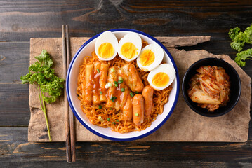Korean spicy instant noodle with Tteokbokki, sausage and egg on wooden background, Table top view