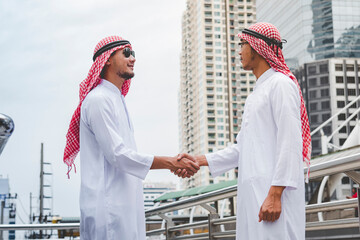 Arab Businessman Muslim dress shaking hands together in modern city UAE background. Muslim Men...