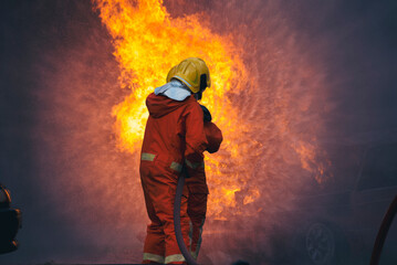 Firefighter fighting with flame using fire hose chemical water foam spray engine. Fireman wear hard...