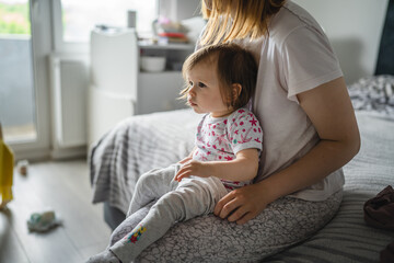 One small caucasian girl toddler sitting on the bed at home while her mother is changing her clothes real people growing up copy space