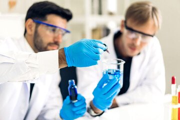 Professional two scientist man research and working doing a chemical experiment while making analyzing and mixing liquid in test tube.Young science man dropping sample chemical on glass at laboratory