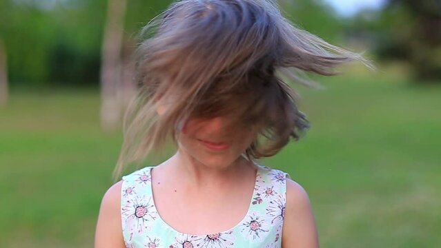 Child cheerful girl happily shakes head with her cheeks painted in the flag of France, her hair flying in different directions. Slow motion funny laughing little blonde kid girl 6-8 years old outdoor