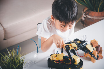 Happy Asian little kid boy using screwdriver to fixes screws robotic machine arm in home workshop, child learning repairing get lesson control robot arm, Technology future science education concept