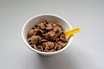 Selective focus image of Wheat & chocolate based cereal flakes in a white bowl with yellow spoon. Food ready to eat.