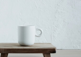 beige ceramic mug on a brown wooden board in front of a white textured wall. copy space. Minimal food concept neutral colors