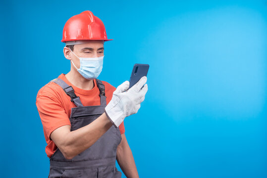 Male builder in face mask using smartphone during work