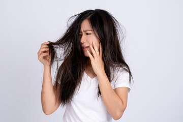 Sad Asian woman looking at her damaged hair with shock standing alone on white background. She used her hand to touch her face.