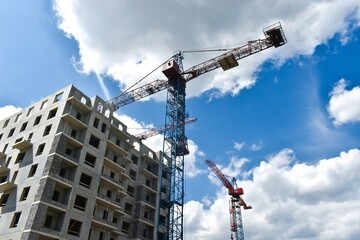 Construction work site. The construction process of a residential house. High-rise cranes against the background of new buildings. New residential buildings construction. Blue sky background, clouds