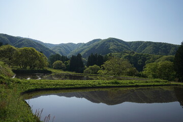 Fototapeta na wymiar 日本の青鬼集落。周囲を山に囲まれた場所で、田んぼや畑が広がる風景。田植えが始まる時期、朝の光で水鏡が美しい。