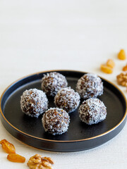 Healthy homemade energy balls: dry fruit ball cakes made from raisin, prune, dates, walnut, figs in black plate against white background, covered with coconut flakes. Close up copy space vertical