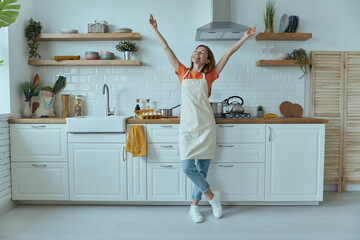 Full length of beautiful young woman looking happy while standing at the domestic kitchen