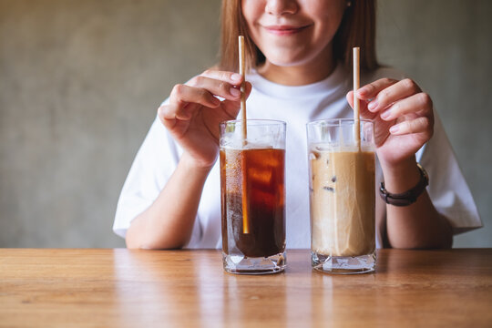 Closeup image of a young woman holding and drinking two glasses of iced coffee