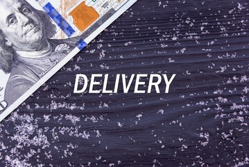DELIVERY - word (text) on a dark wooden background, money, dollars and snow. Business concept (copy space).