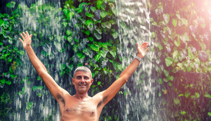 Happy man embracing nature under a beautiful waterfall.