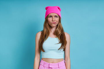 Young woman in pink hat looking displeased while standing against blue background