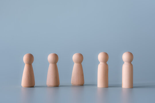 Group of wooden human figures standing in community society concept. Wooden dolls on light blue background.