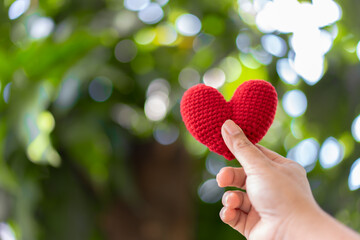 Hand holding red yarn heart shape with natural beauty background in sunny day.