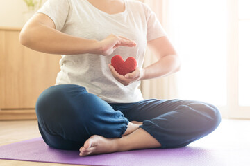 Woman hold red yarn heart shape in hand doing yoga post at home. Yoga is good for heart -...