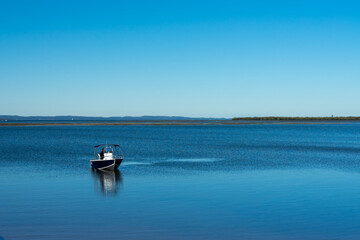 Fototapeta na wymiar Minimalist scene: single motorboat on calm blue water, Stradbroke Island on the horizon, and clear blue sky. Wellington Point, Queensland, Australia 