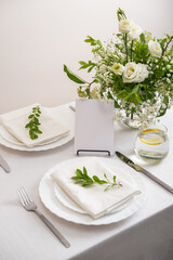 Mockup white blank space card for table number or menu. Wedding teble decoration with white flowers, glasses and white napkins. Elegantly decorated table at a wedding reception. 
