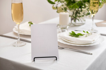 Mockup white blank space card for table number or menu. Wedding teble decoration with white flowers, glasses and white napkins. Elegantly decorated table at a wedding reception. 