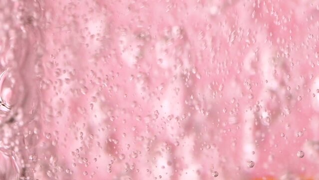 Slow motion close-up pouring water in glass on pink rose background with bubbles