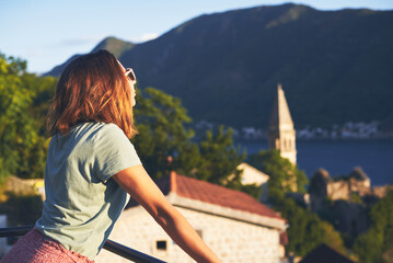 Fototapeta na wymiar Woman in summer vacation. Young woman enjoy sunset on balcony in small old town on seaside in Montenegro looking at view on sea.