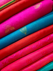 Closeup view of stacked colours saris or sarees in display of Indian retail shop, textile shop.