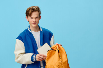 cute trendy guy in a bomber jacket holding an orange backpack tucking a notepad into it