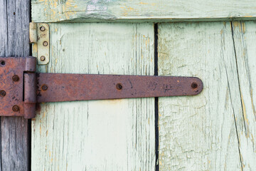 Ancient wooden door background. Fragment of old gate with remnants of green paint and rusty hinges
