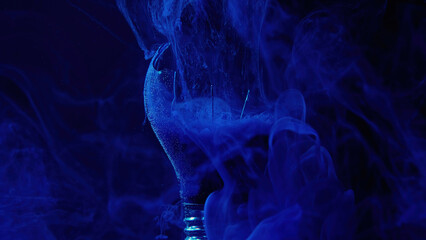 Ink water floating. Smoke cloud. Underwater explosion. Navy blue color gas in broken light bulb glass on dark conceptual abstract art background.