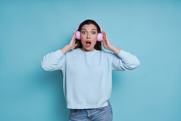 Surprised young woman in headphones listening music and looking at camera