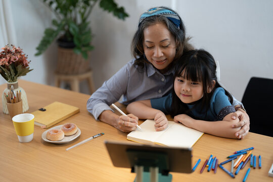Smiling senior grandma and cute little kid granddaughter watching cartoons on laptop together, happy older grandmother grawing and painting.