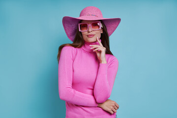 Beautiful woman in pink hat holding hand on chin while standing against blue background