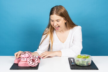 Happy surprised pretty young woman looking at candy. Choosing chocolate donuts instead of salad or...