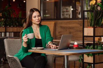 Female blogger or freelancer drinking coffee and working with a laptop in the cafe or coworking area