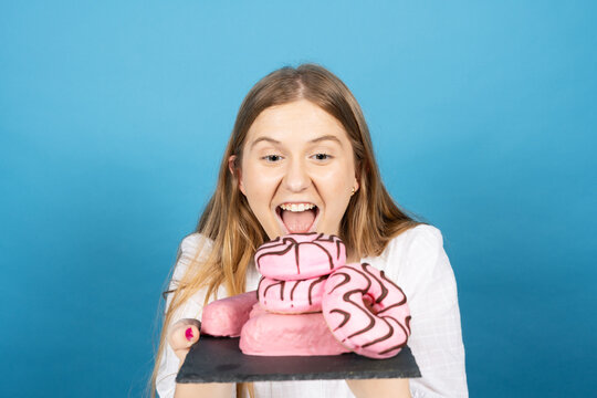 Young Woman Holding Pile Of Candy Sweet Food With Envy Isolated On Blue Background.. Bad Eating Habits Concept.